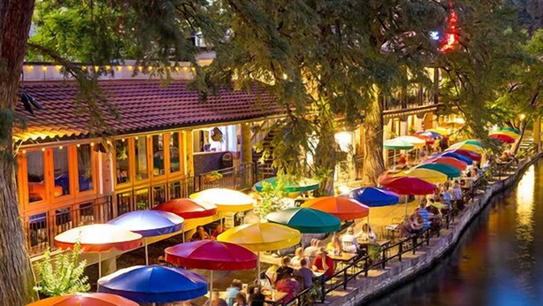 Un restaurante a la orilla del río con terraza y sombrillas de colores.