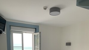 Una camera da letto con un letto, un tavolino, una finestra vista oceano e una lampada a soffitto.