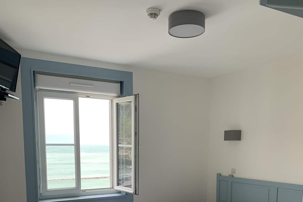 Een slaapkamer met een bed, een klein tafeltje, een raam met uitzicht op de oceaan en een plafondlamp.