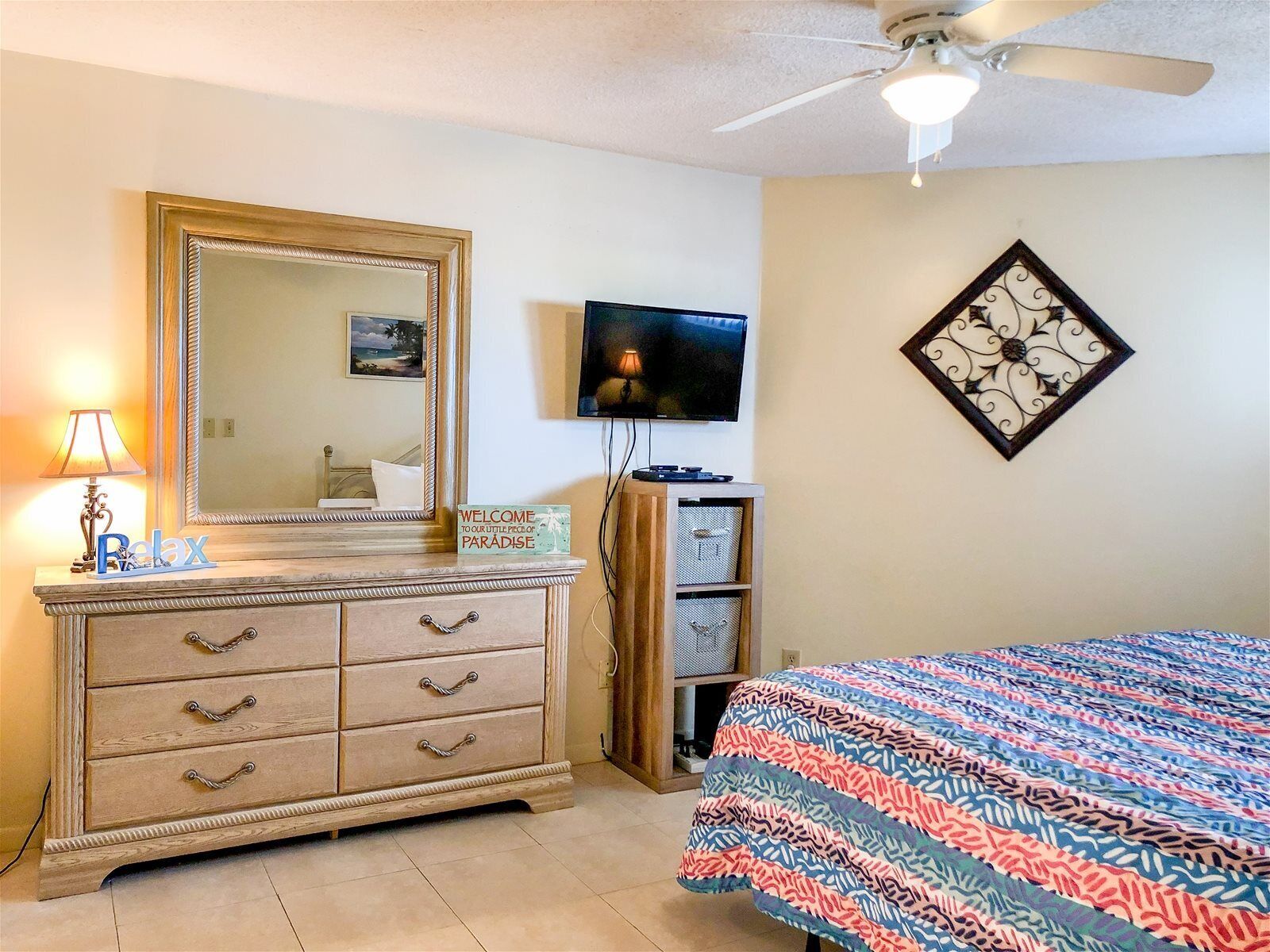 Quarto com cama, cômoda, televisão e ventilador de teto.