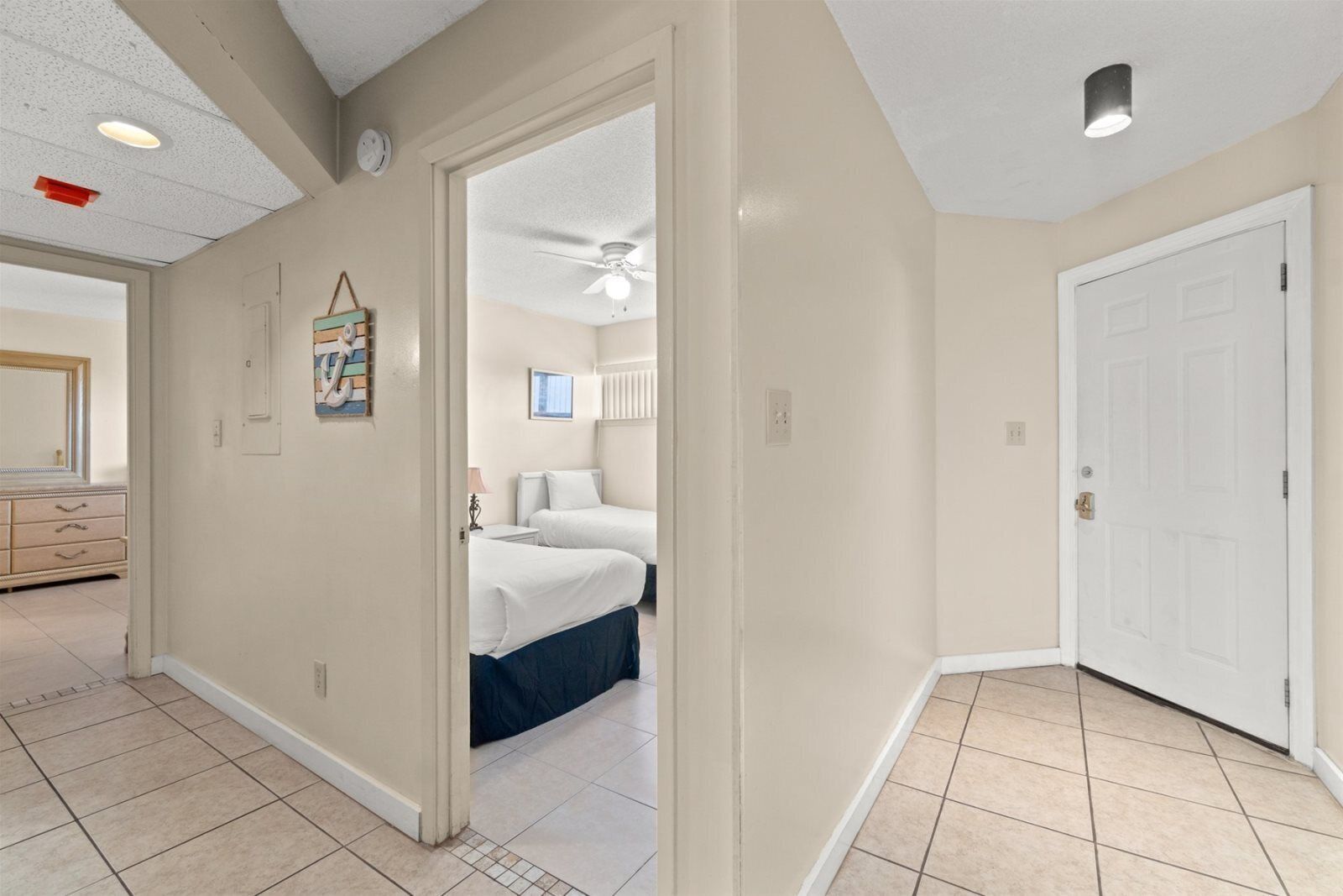 Une chambre avec deux lits, un ventilateur de plafond et une porte donnant sur une autre pièce.