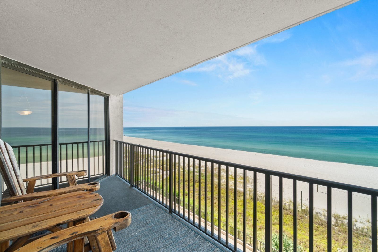 A balcony with a view of the ocean, wooden chairs, and a table.