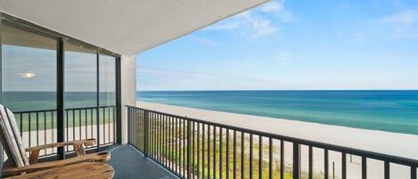 A balcony with a view of the ocean, wooden chairs, and a table.