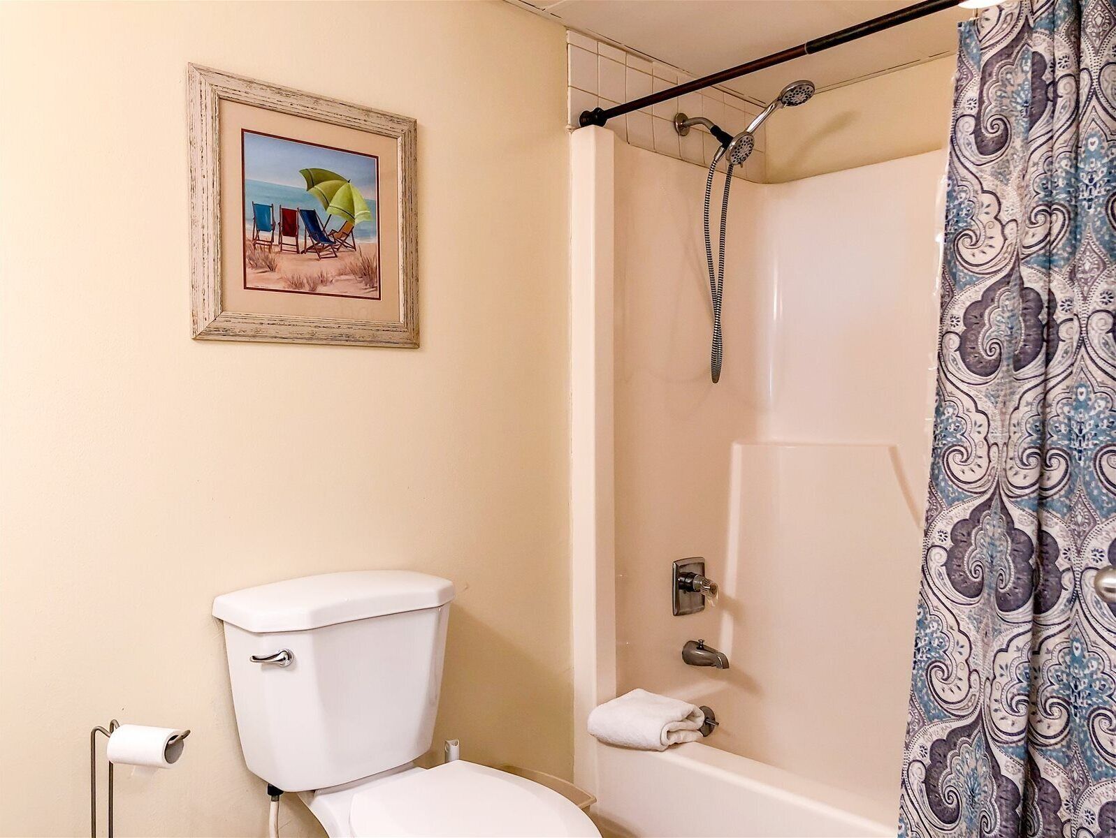 Un baño con inodoro, ducha y un cuadro de playa enmarcado en la pared.
