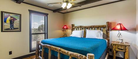 Une chambre à coucher avec un lit en bois, un ventilateur de plafond, une fenêtre avec des stores et deux lampes de chevet.