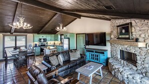 Un intérieur rustique avec une cheminée en pierre, un canapé en cuir, un coin repas et une cuisine aux armoires de couleur turquoise.