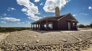 Un chalet rustique doté d’un patio couvert, entouré d’une zone recouverte de gravier et d’une végétation clairsemée.