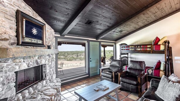 Un intérieur chaleureux avec une cheminée en pierre, des fauteuils en cuir et une vue sur l’extérieur.