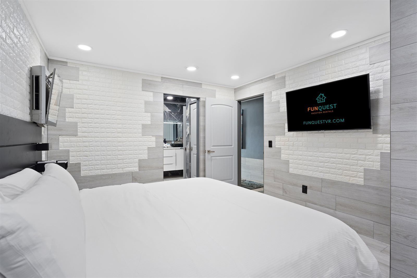 A modern hotel room with a large bed, a TV mounted on the wall, and a bathroom visible through an open door.