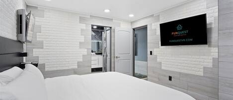 A modern hotel room with a large bed, a TV mounted on the wall, and a bathroom visible through an open door.