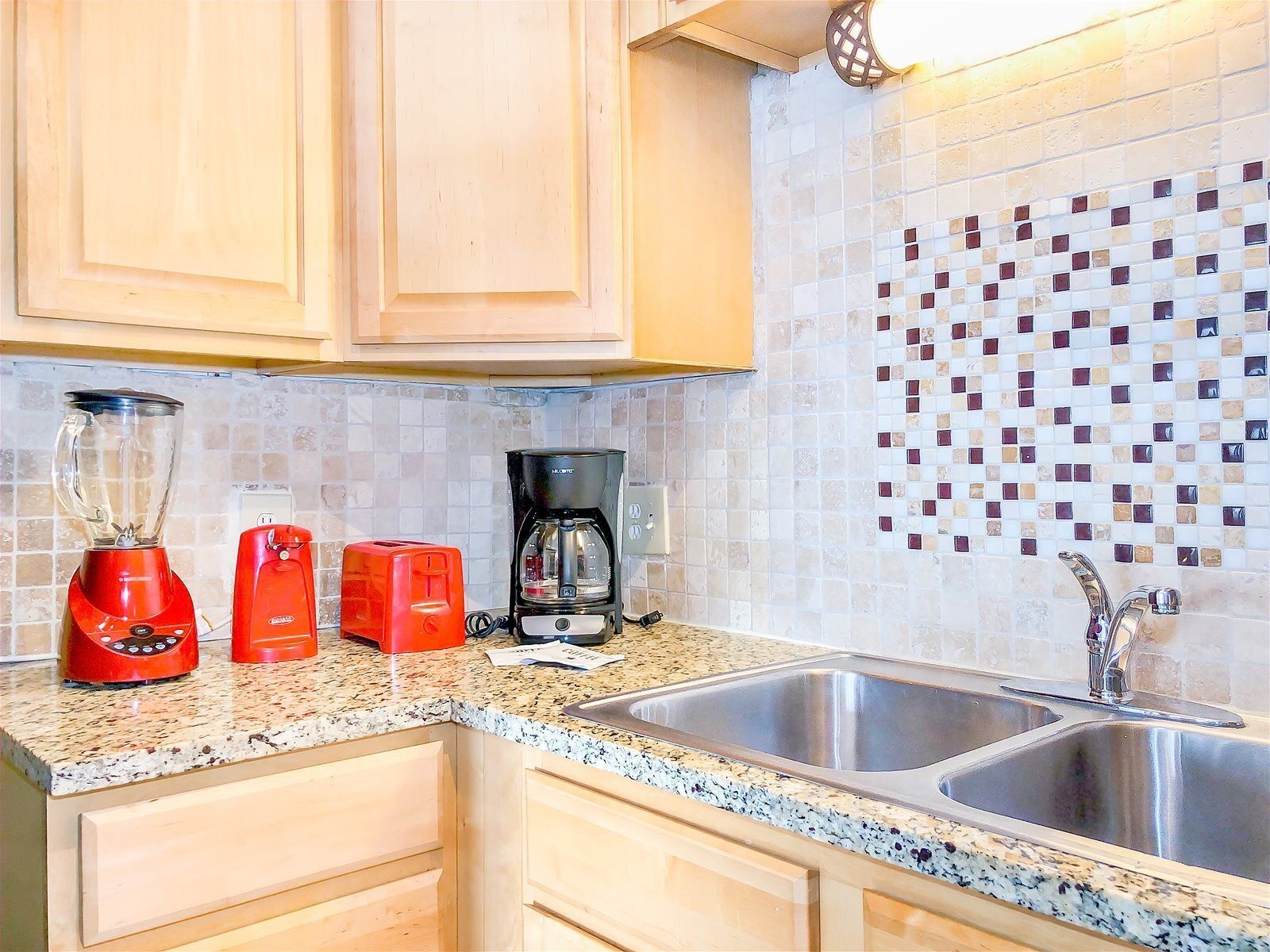 A kitchen with wooden cabinets, a granite countertop, a double sink, a coffee maker, and a blender.