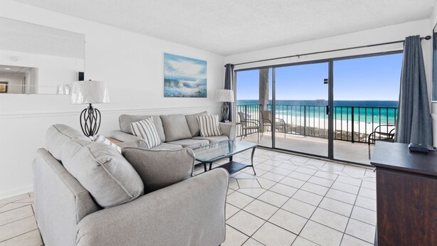 A modern living room with a grey sofa, a glass coffee table, and a view of the beach through large sliding doors.