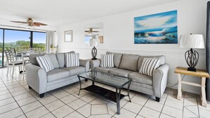 A modern living room with a grey sectional sofa, a glass coffee table, and a view of the outdoors.