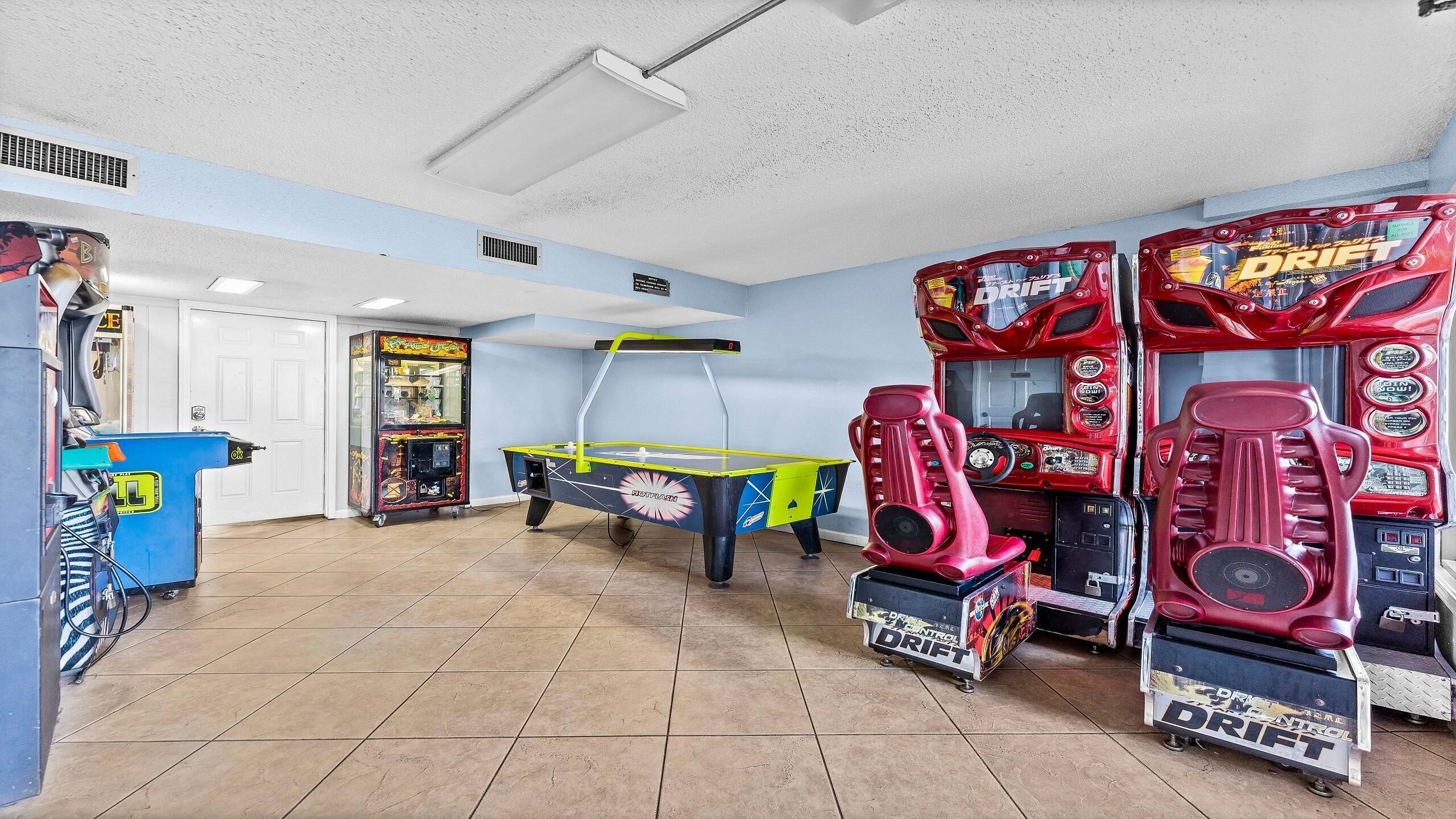 Una habitación con juegos de arcade, una mesa de ping pong y una máquina expendedora azul.