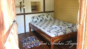 A room with a bed, a wooden floor, a mirror, and a wall-mounted fan. - Cabinas Manawada (Puerto Jiménez)