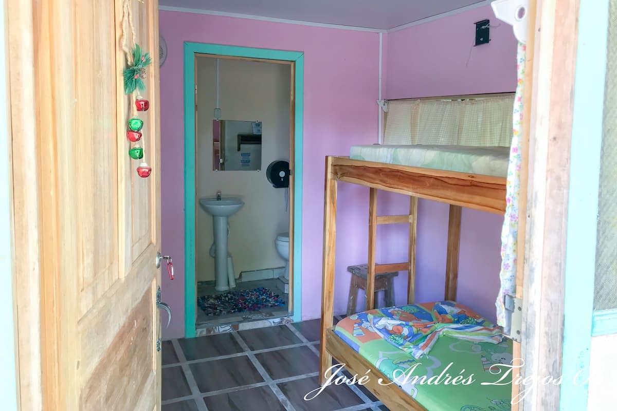 Une petite pièce, de taille modeste, avec un lit superposé, un bureau en bois, un lavabo et un miroir dans un coin.