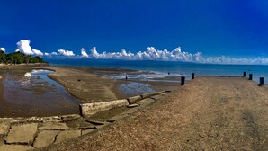 A beach with a concrete walkway leading to the water, a clear sky, and a distant view of the ocean. - Cabinas Manawada (Puerto Jiménez)