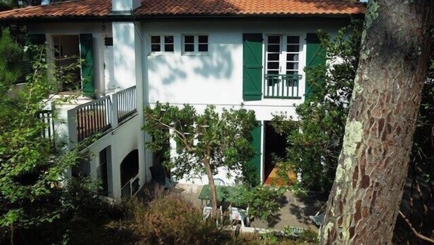 A two-story house with a tiled roof, green shutters, and a white exterior.