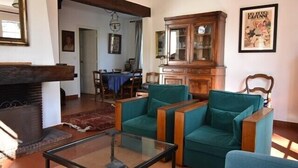 A living room with teal armchairs, a glass coffee table, a wooden cabinet, and a fireplace.