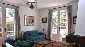 A living room with a blue sofa, a glass coffee table, and a piano.