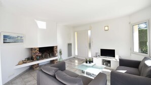 Un salon moderne avec une cheminée, des canapés gris, une table basse en verre et un téléviseur à écran plat.