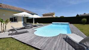 Un jardin avec une piscine, des chaises longues et des parasols.