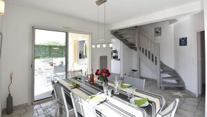 Un coin repas avec une table dressée pour quatre personnes, un escalier et une porte donnant sur l’extérieur.