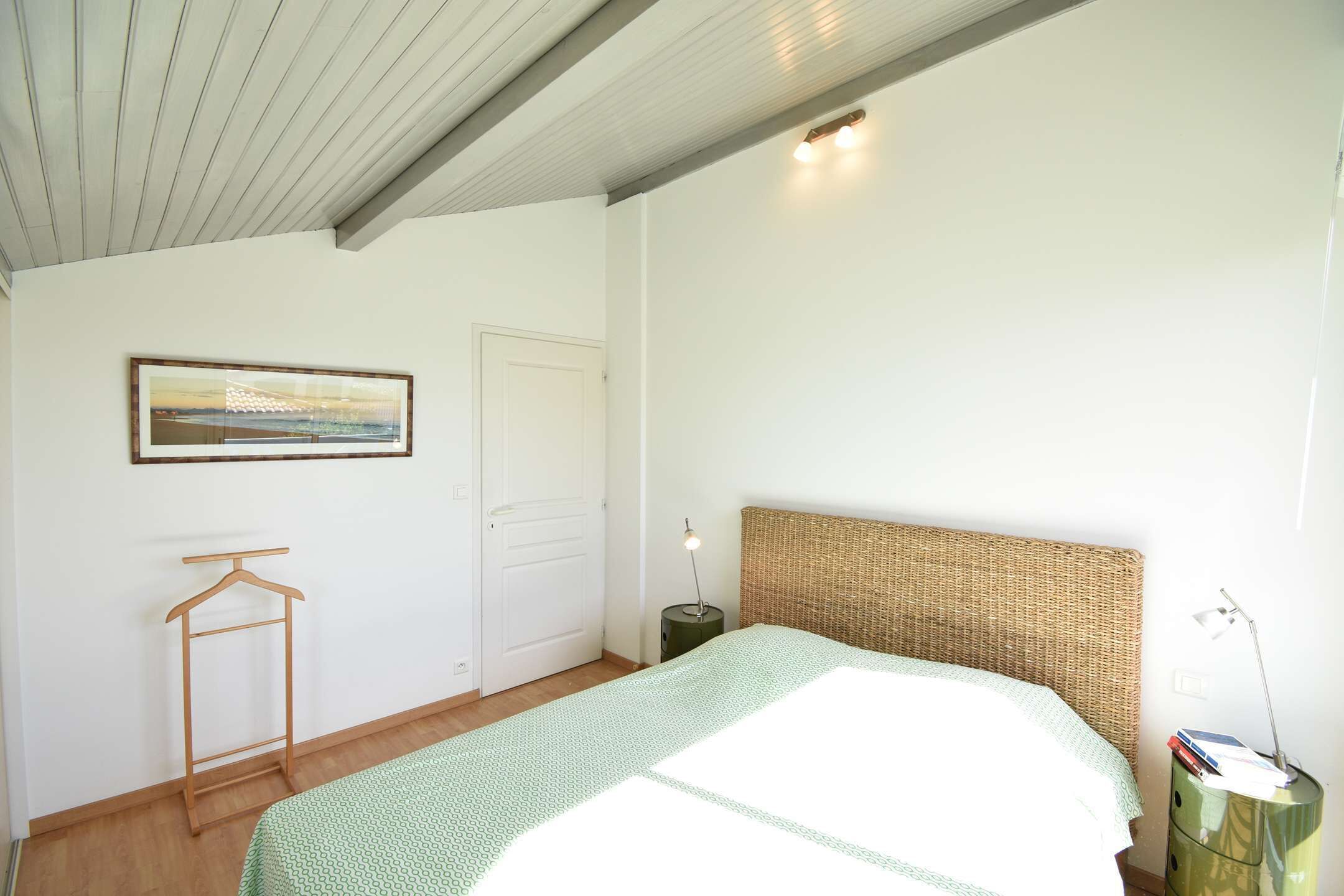 A bedroom with a bed, a hanging clothes rack, a bedside table with a lamp, and a door.