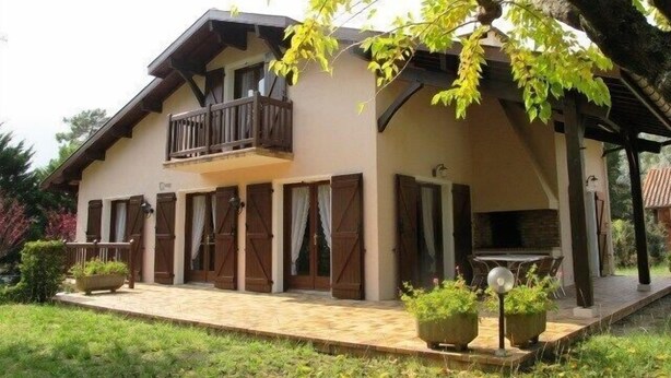 A two-story building with a balcony, wooden shutters, and a covered porch area.