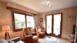 A living room with a sofa, two armchairs, a coffee table, and large windows with curtains.