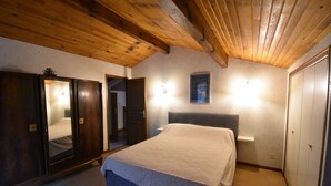 A bedroom with a wooden ceiling, a bed with a headboard, a wardrobe, and a mirror.