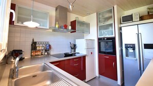 A kitchen with a stainless steel sink, red cabinets, a white refrigerator, and a microwave on top.