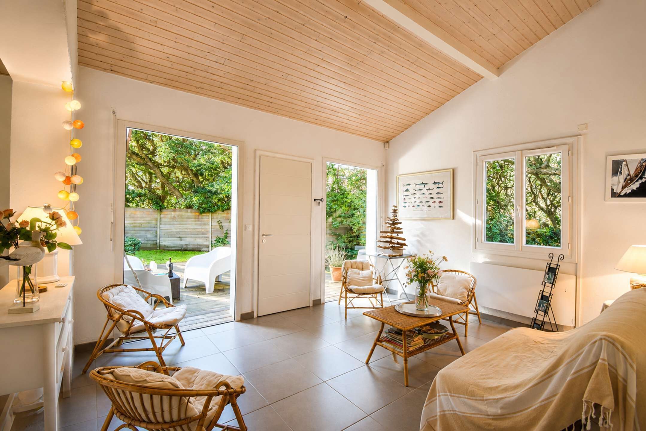 A spacious living area with a wooden ceiling, large windows, and a view of the garden.