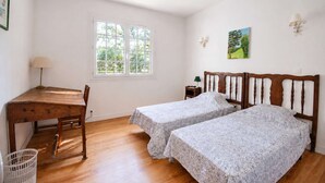 Une chambre avec un bureau en bois, deux lits simples, une fenêtre et une lampe fixée au mur.