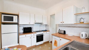 Une cuisine compacte avec des meubles blancs, un four à micro-ondes, un grille-pain et une bouilloire.