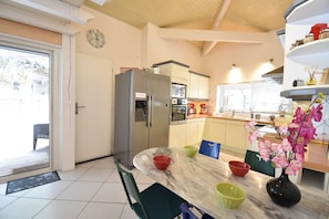 Una cocina moderna con refrigerador, horno y microondas. Hay una mesa de comedor con sillas y un florero con flores.