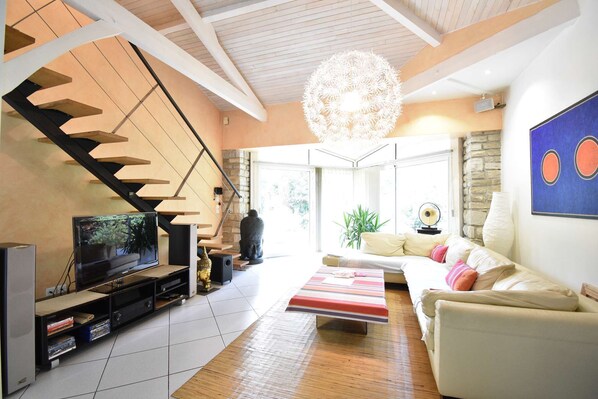 A modern living room with a staircase, a flat-screen TV, a sofa, and a decorative chandelier. - Hossegor “Thaïs”, Pleasant villa with swimming pool for 8 people. (Soorts-Hossegor)