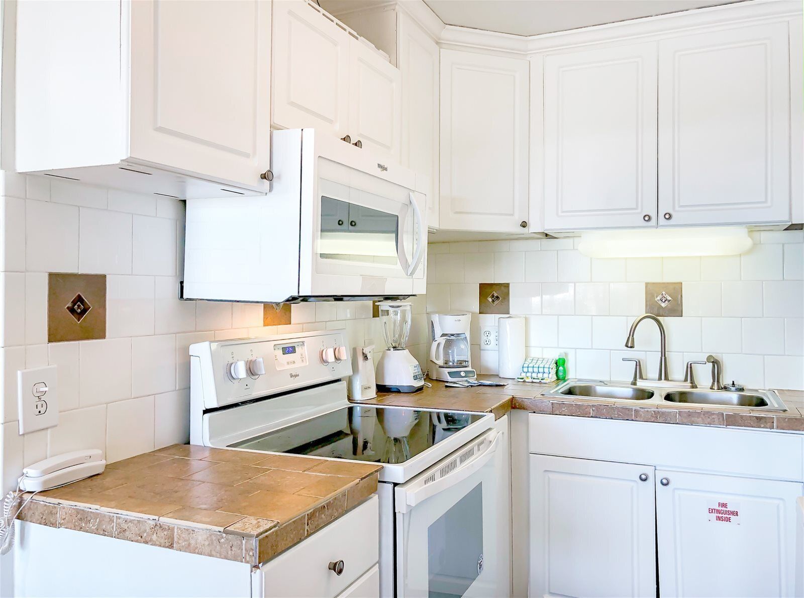 A modern kitchen with white cabinets, a built-in oven, microwave, and a coffee maker.