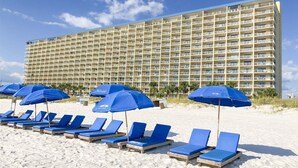 Un hôtel doté de nombreux balcons et d’un espace plage avec des transats et des parasols.