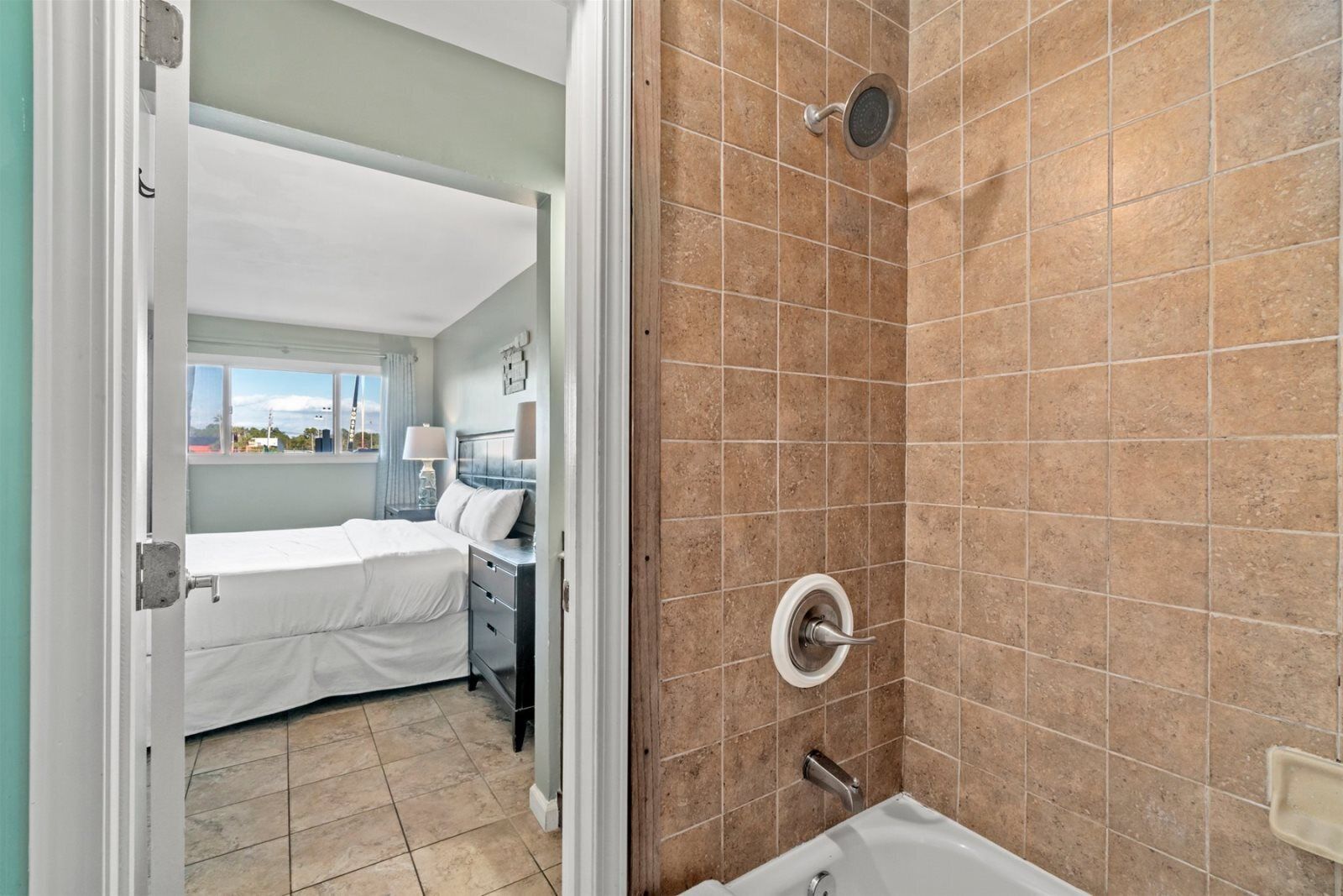 A hotel room with a bed, a desk, a window, and a shower area.