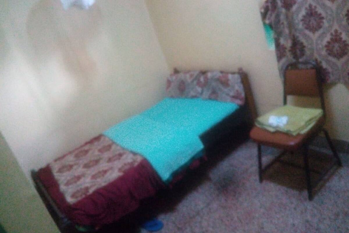 A small, single-bed room with a patterned bedspread, a chair, and a small table.