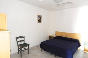 A bedroom with a bed, a chair, a nightstand, and a small table.