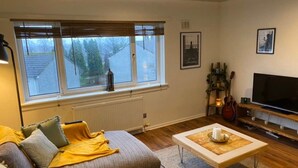 A cozy living room with a sofa, a coffee table, a TV, and a window with blinds.