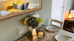 A dining table set with plates, glasses, and cutlery, a vase with flowers, and a mirror above.