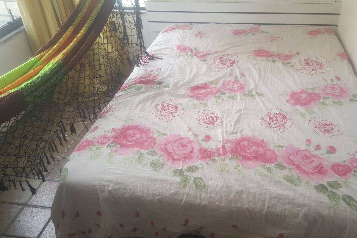 A bed with a floral bedspread, a netted hammock, and a window with curtains.