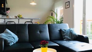 Uma sala de estar moderna com um sofá seccional preto, uma pequena mesa lateral com um vaso amarelo e uma grande janela que oferece luz natural.