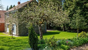 Une maison en pierre dotée d’un jardin bien entretenu, comprenant une pelouse et des plantes à fleurs.