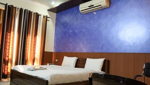 Een hotelkamer met een bed, een stoel, een airconditioner en een raam met gordijnen.