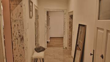 Un couloir avec un banc, un miroir appuyé contre un mur et une porte ornée d’un cadre décoratif.