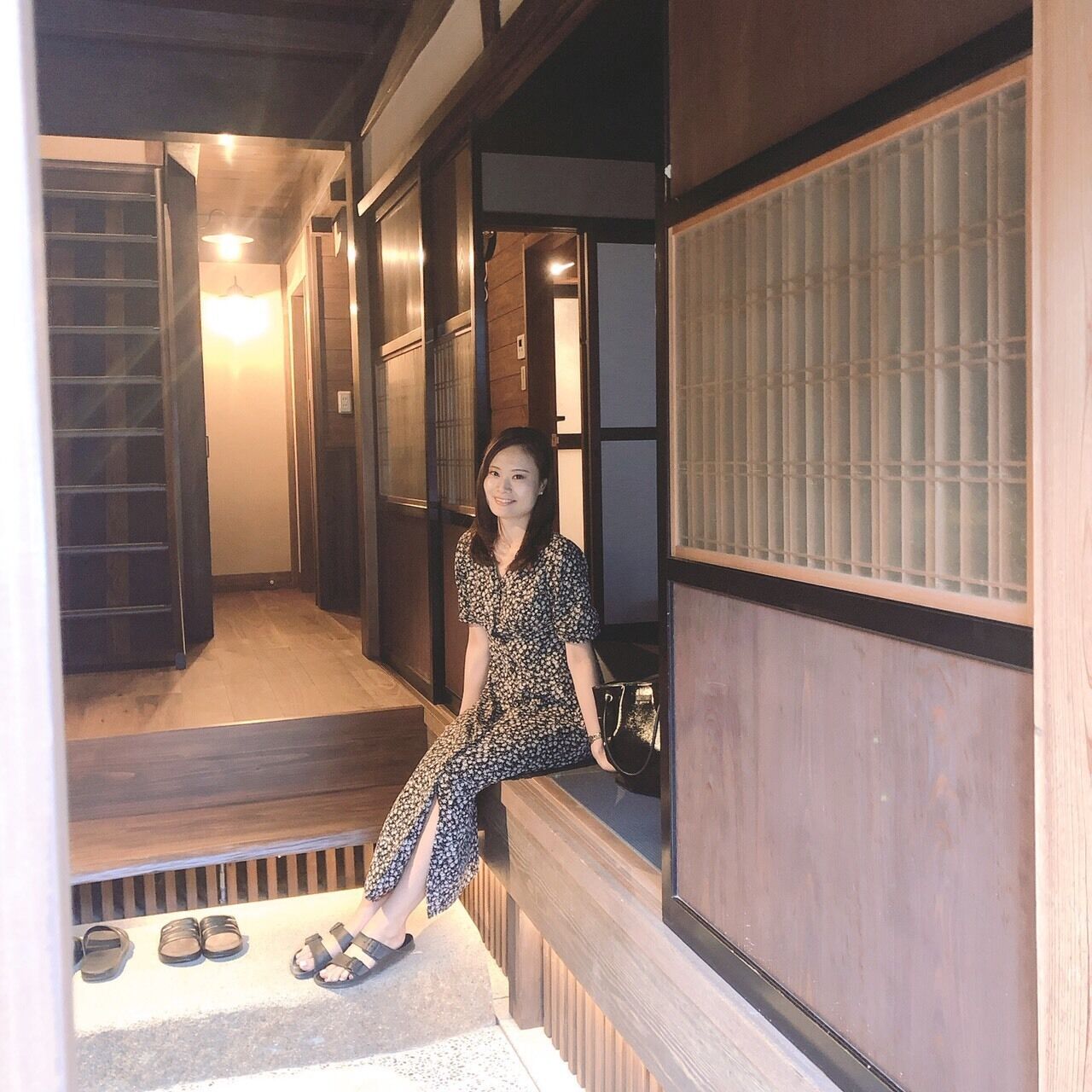 A traditional Japanese interior with sliding doors, a wooden floor, and a person sitting on a bench.